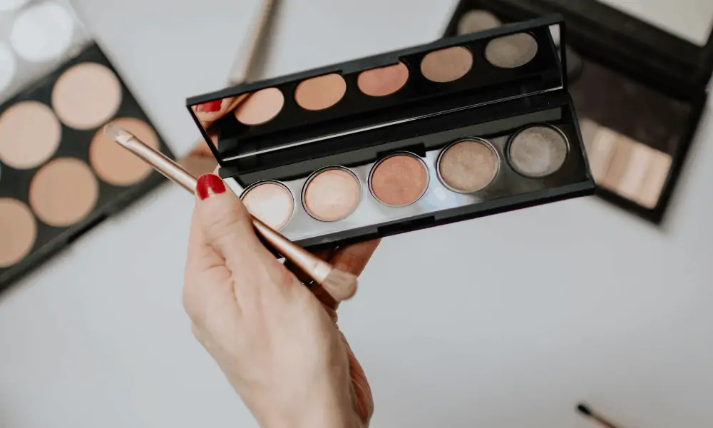A person holding a makeup palette consisting of neutral tones. 