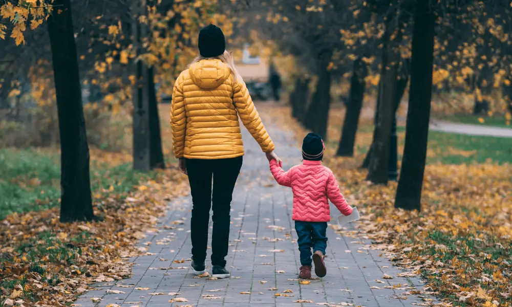 Woman walking with daughter on a path during the fall time. 