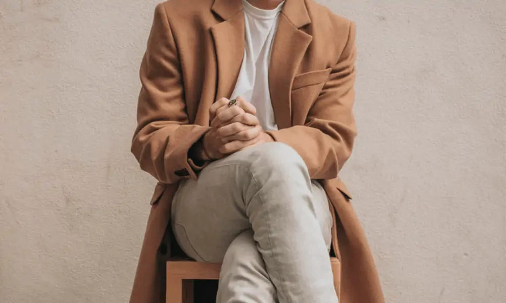 Man wearing a camel coat, a white t-shirt, and light wash jeans. A good example of sustainable and minimalist outfit. 