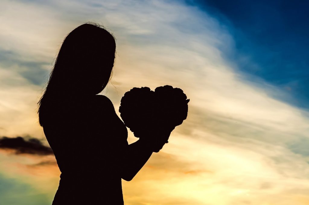 sunset with shadow outline of girl holding a heart