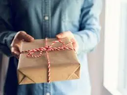 photo of man in blue collared shirt holding a package wrapped in white and red string